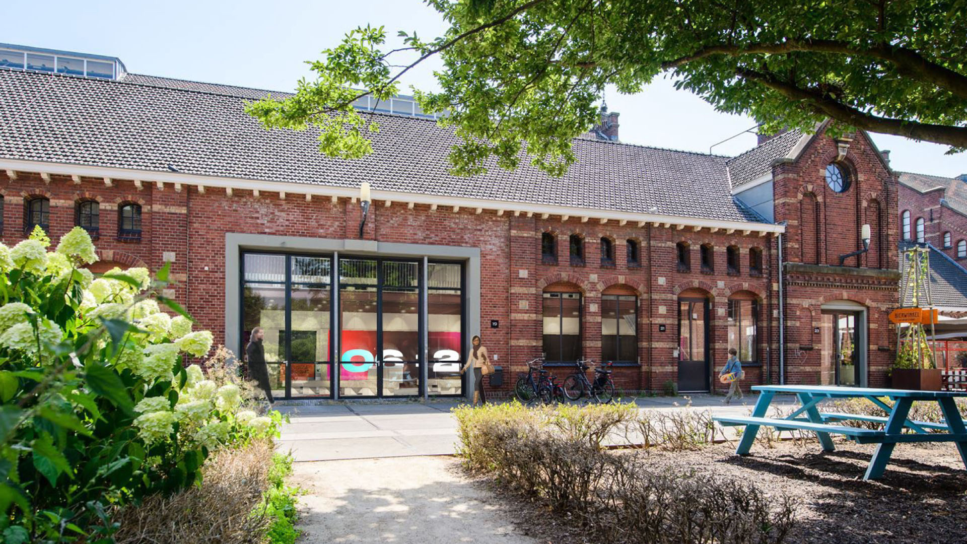 Buitenaanzicht van een rood bakstenen gebouw in de Westergasfabriek in Amsterdam, met grote glazen ramen en traditionele architectuur